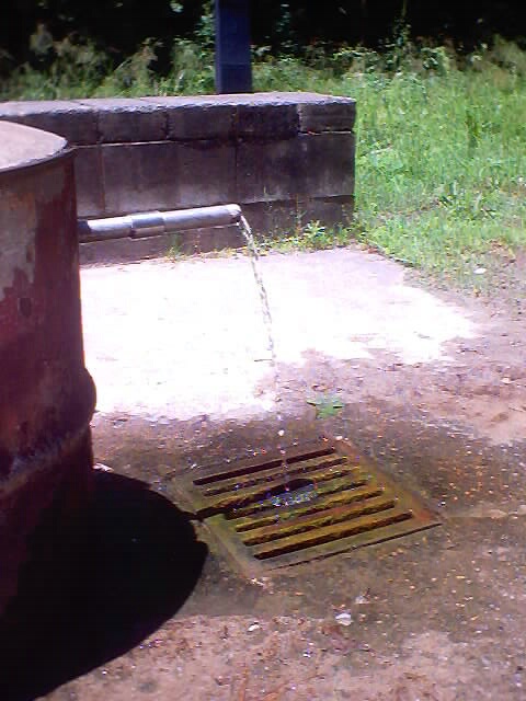Water spills from the end of a horizontal pipe attached to the wellhead.