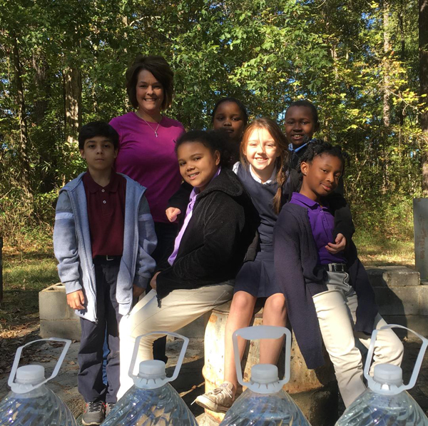 Group photo of a teacher with 6 students. Four jugs of water in foreground.