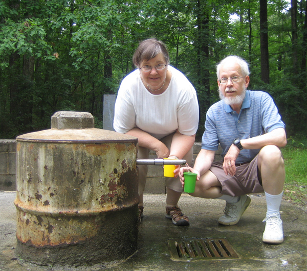 A couple squats at the side of the spring, filling drinking cups.